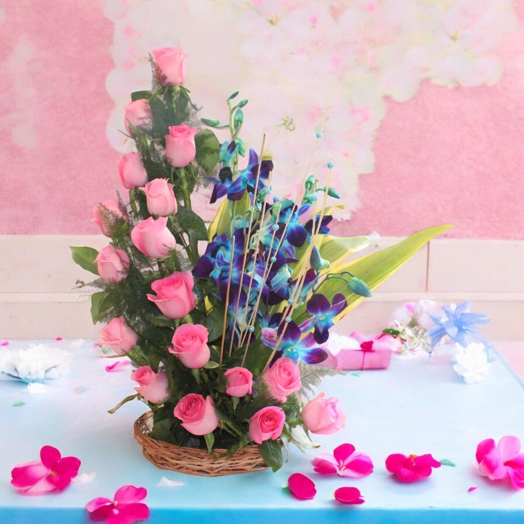 A beautiful arrangement of 18 pink roses and 3 blue orchids in a wicker basket by BetterGiftFlowers.