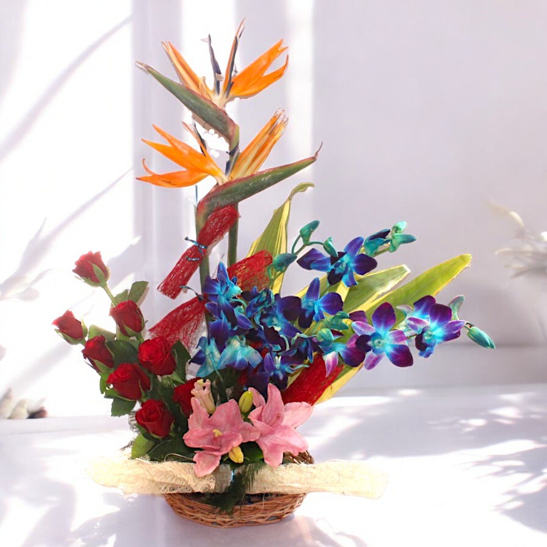 An unforgettable moment premium flower arrangement by BetterGiftFlowers featuring red roses, blue orchids, pink lilies, and birds of paradise in a decorative basket.