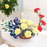 BetterGiftFlowers "Exquisite Arrangement" with yellow carnations, red carnations, and blue orchids in a basket.