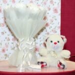 White Beauty combo of fresh white carnations and a teddy by BetterGiftFlowers displayed on a wooden surface.