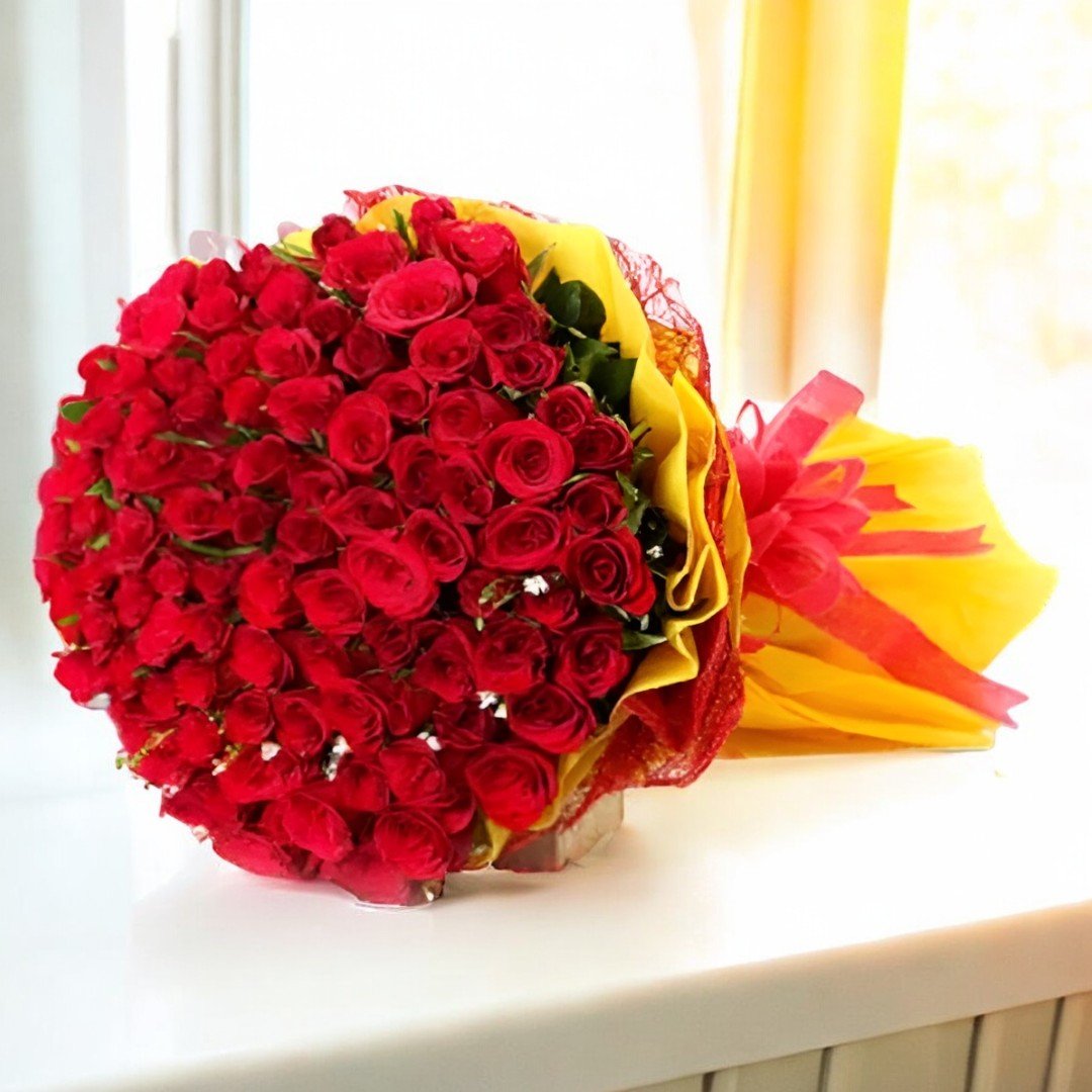 BetterGiftFlowers Addicted bouquet of 100 fresh red roses wrapped in vibrant yellow and red paper placed near a window.