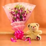 Purple Orchid Bouquet and Teddy from BetterGiftFlowers placed on a table.