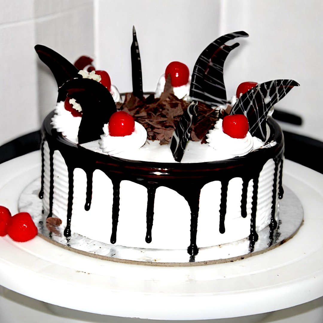 BetterGiftFlowers Black Forest Cherry Cake topped with cherries and chocolate decorations on a white cake stand.