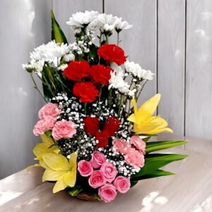 BetterGiftFlowers handcrafted floral basket with red carnations, pink roses, yellow lilies, and white chrysanthemums on a wooden table.