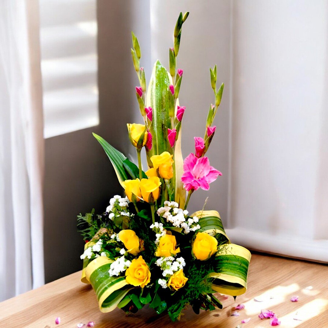 A vibrant yellow rose and pink gladiolus basket arrangement by BetterGiftFlowers, displayed on a wooden table with natural light.